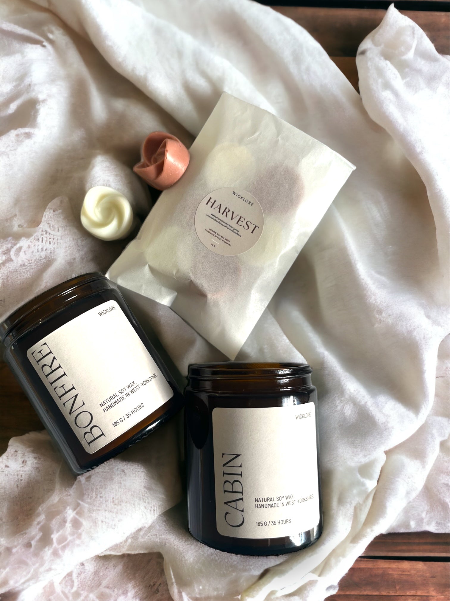 Scented candles and wax melt pack arranged in a flat lay on a brown table with white cloth